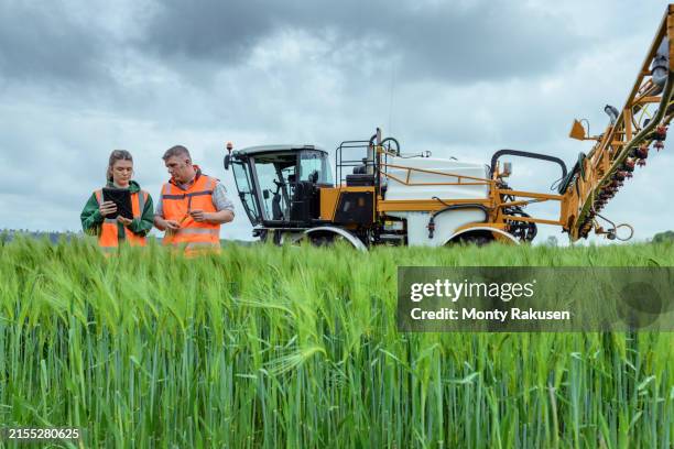 farmers inspecting gps (global positioning system) and soil condition data on tablet in front of crop sprayer on farm - agriculture photos et images de collection