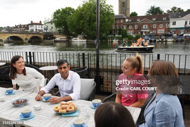 Boat of Liberal Democrat supporters passes by on the river as Britain's Prime Minister and Conservative Party leader Rishi Sunak enjoys a warm drink...