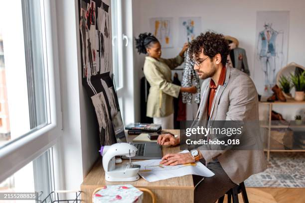 jeune tailleur utilisant un ordinateur portable pour travailler dans son atelier. - industrie de la mode photos et images de collection