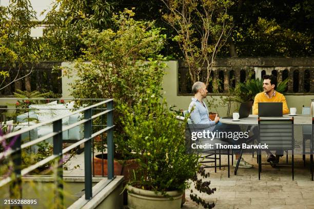 wide shot view couple working on laptops on deck of boutique hotel - rooftop deck stock pictures, royalty-free photos & images
