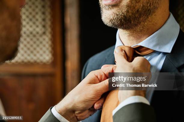 close up shot man helping husband tie necktie in bedroom of hotel - completo da uomo foto e immagini stock