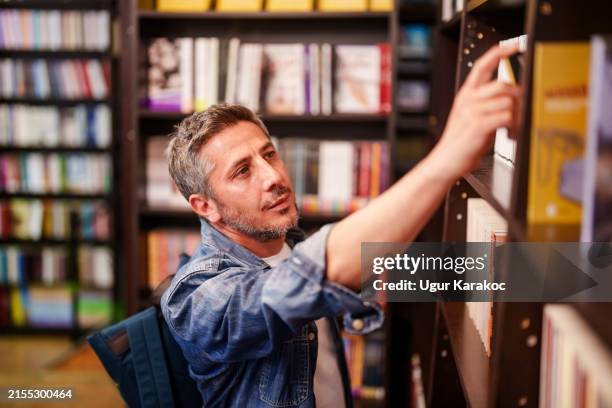mann untersucht die bücher in den regalen der buchhandlungen. - öffentliche bibliothek stock-fotos und bilder