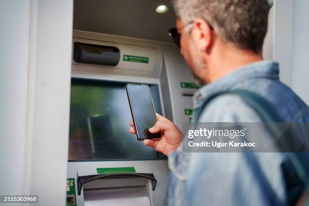 un hombre está retirando dinero de un cajero automático con un teléfono móvil, un código qr. - quitar fondo de imagen online fotografías e imágenes de stock
