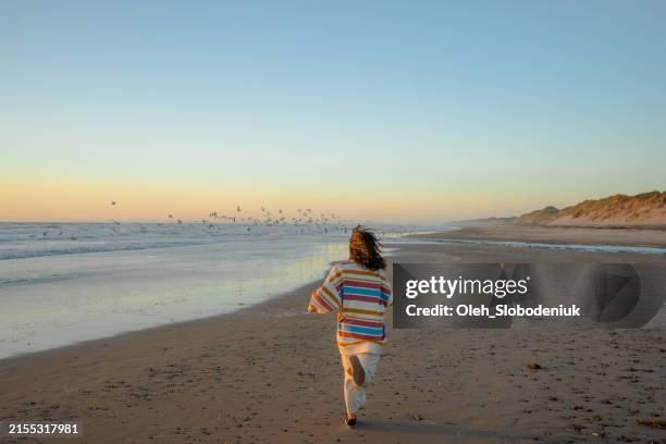 carefree woman running on the north sea beach at sunset - noordzee stockfoto's en -beelden