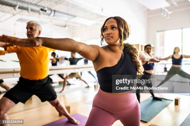 diverse group of yoga students doing warrior pose in yoga class - fitness photos et images de collection