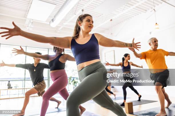 diverse group of yoga students doing warrior pose in yoga class - activité physique photos et images de collection