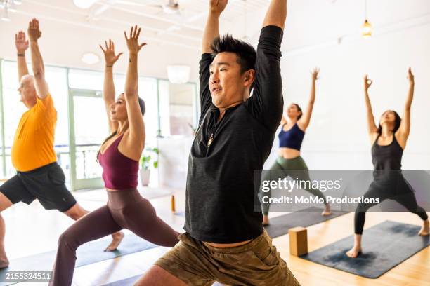 diverse group of students doing crescent lunge pose during yoga class - fitness en wellness stockfoto's en -beelden