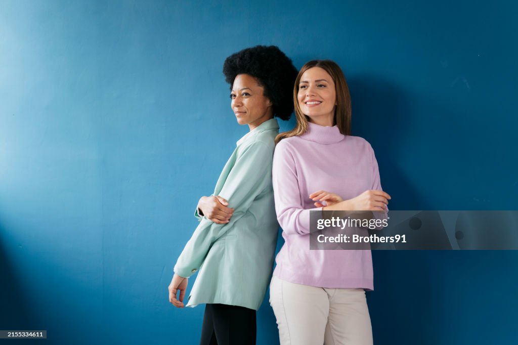 Two confident businesswomen standing back to back looking away