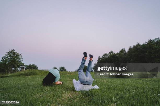 low section of fallen young couple rolling on grass against clear sky at sunset - summer solstice stock pictures, royalty-free photos & images