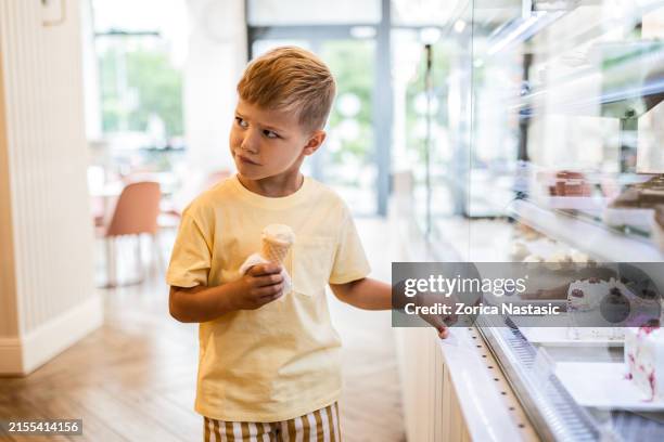 kleiner junge zeigt auf kuchen, während er eine eistüte genießt - ungezogenes kind stock-fotos und bilder