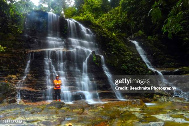 scenic view of kubah waterfall with female hiker for scale in kubah national park in kuching, sarawak, malaysia - sarawak state stock pictures, royalty-free photos & images