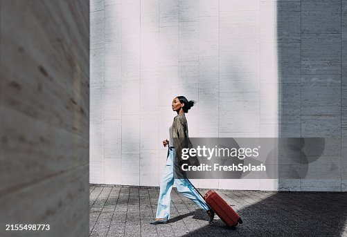 Donna fiduciosa che cammina con la valigia rossa in un ambiente urbano moderno Donna fiduciosa che cammina con la valigia rossa in un ambiente urbano moderno