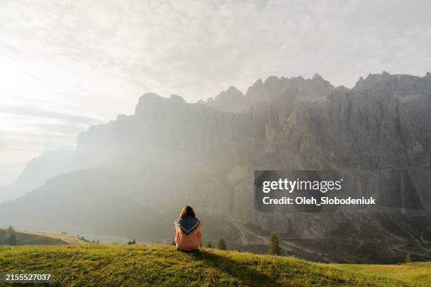 woman sitting on mountain top looking at view of val gardena - effetto luminoso foto e immagini stock