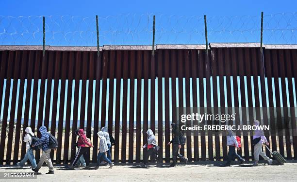 Migrants walk on the US side of the border wall in Jacumba Hot Springs, California on June 5 after crossing from Mexico. Migrants from countries such...