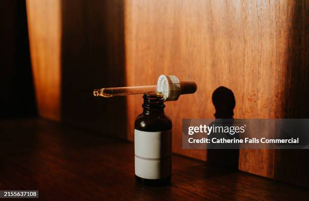 a single bottle on a wooden surface with a pipette balanced on top of it - pipetta foto e immagini stock