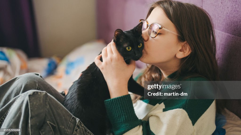 Kid in bed is kissing her cat