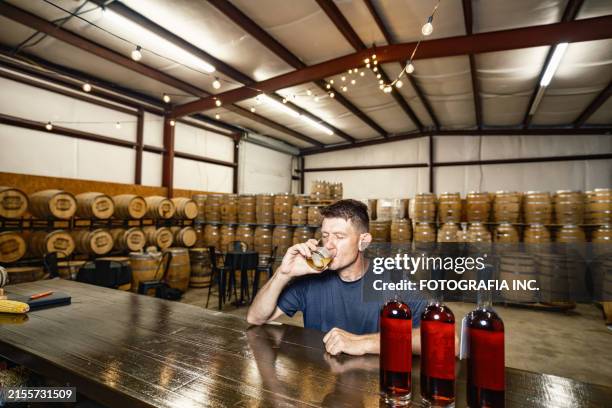 mid adult male whisky distiller tasting his whisky at distillery bar - whiskey tasting stock pictures, royalty-free photos & images