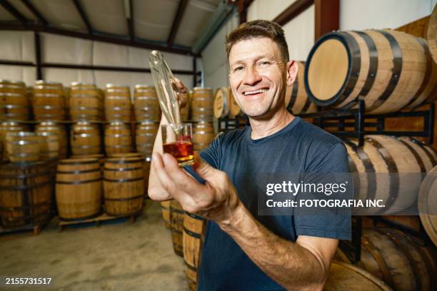 mid adult male whisky distiller tasting his whisky at distillery bar - whiskey tasting stock pictures, royalty-free photos & images