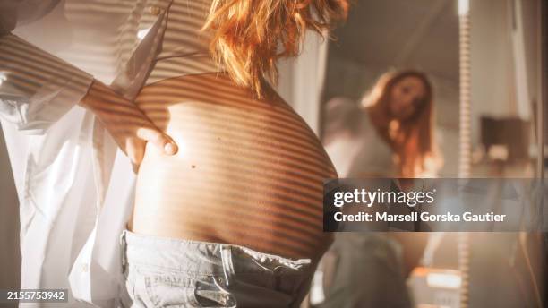 a pregnant woman strokes her belly in front of the mirror. light stripes on the belly. - in front of stock pictures, royalty-free photos & images