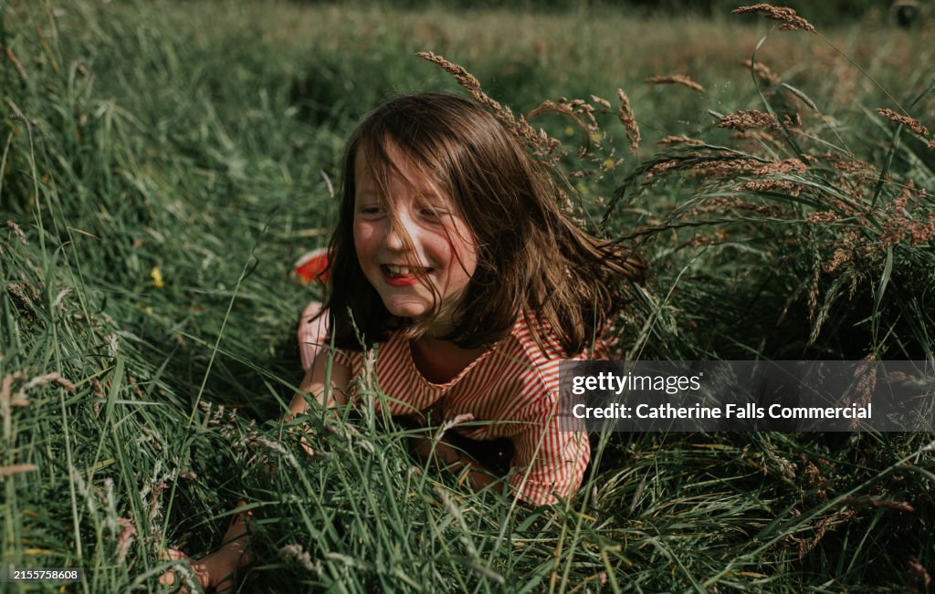 A clumsy little girl throws caution to the wind, tripping as she runs through a field