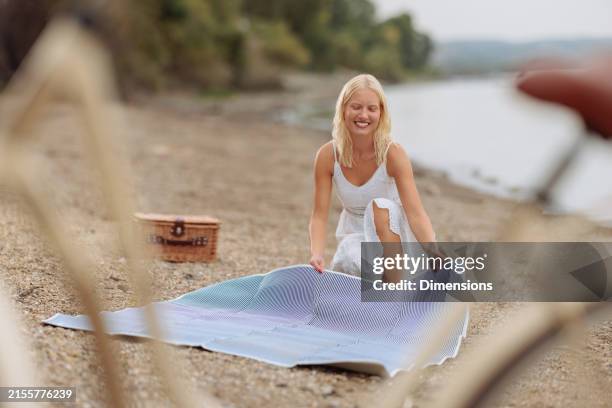 blonde woman setting up a picnic spot - riverside beach stock pictures, royalty-free photos & images