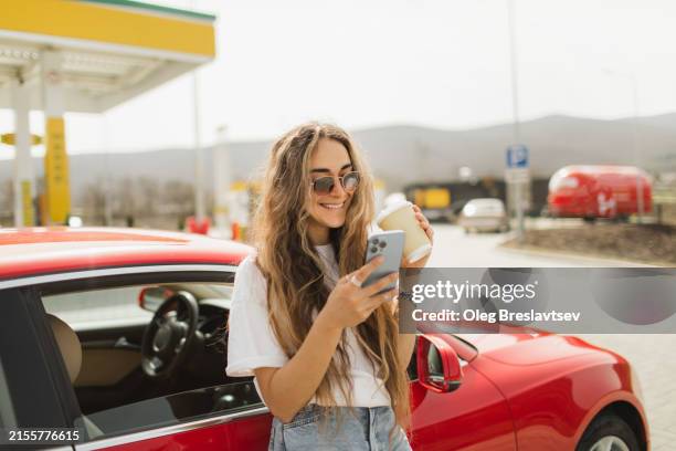 woman taking a break with coffee and mobile phone after driving - gasolinera fotografías e imágenes de stock