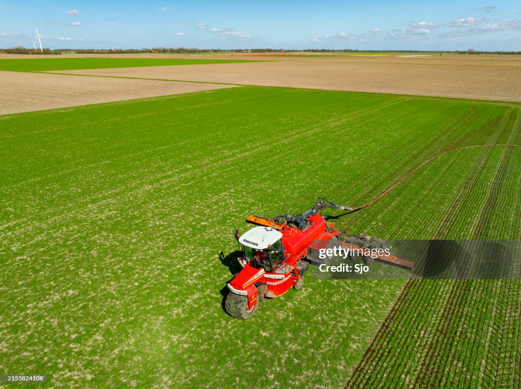 Traktor spritzt Viehgülle in ein Feld von oben gesehen