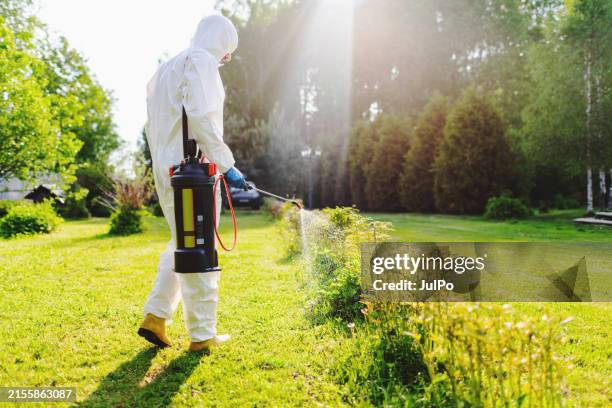 mid adult man in protection suit insecticide spraying the garden - lawn fertilizer stock pictures, royalty-free photos & images