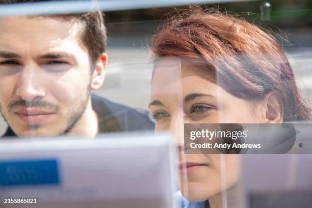 couple looking at property at real estate agent's office - annonce immobilière photos et images de collection