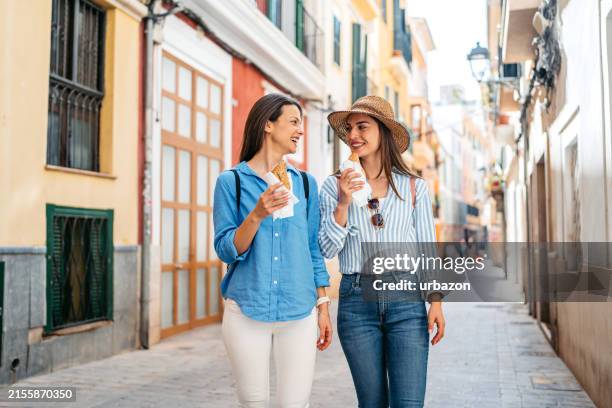 two female friends eating pastry on the street in palma de mallorca in spain - spanish food stock pictures, royalty-free photos & images