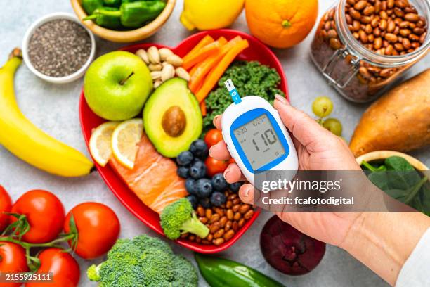 händchenhaltendes blutzuckermessgerät auf gesundem ernährungshintergrund - vorbeugung stock-fotos und bilder