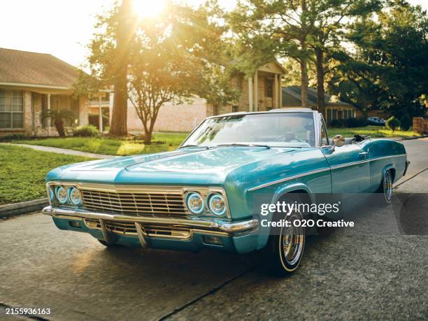 man in a lowrider convertible car cruising in a neighborhood - oldtimerauto stock-fotos und bilder