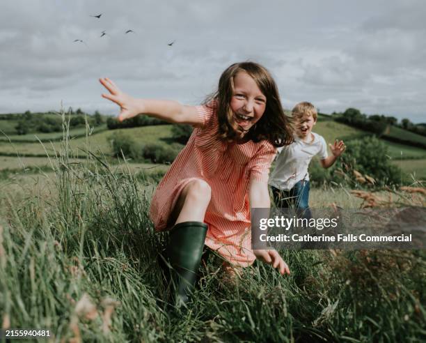 two absolutely joyful children run towards the camera, through a lush, green field on a sunny day - divertirsi foto e immagini stock