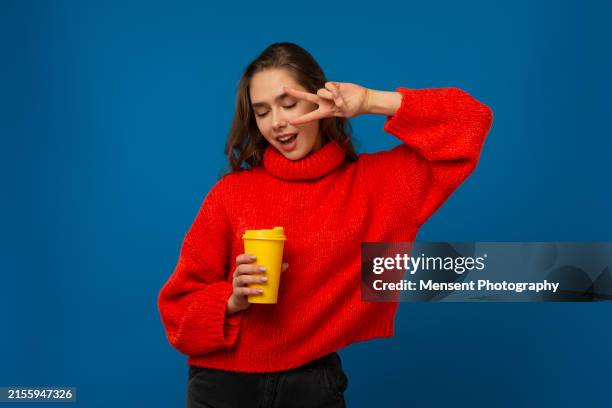 happy young casual woman holding a disposable coffee cup and gesturing in a blue background - travel mug stock pictures, royalty-free photos & images