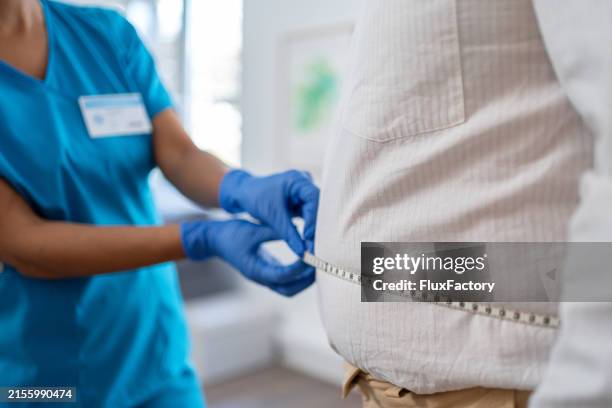 waist measurement in medical practice. the nurse is using a tape measure - överviktig bildbanksfoton och bilder
