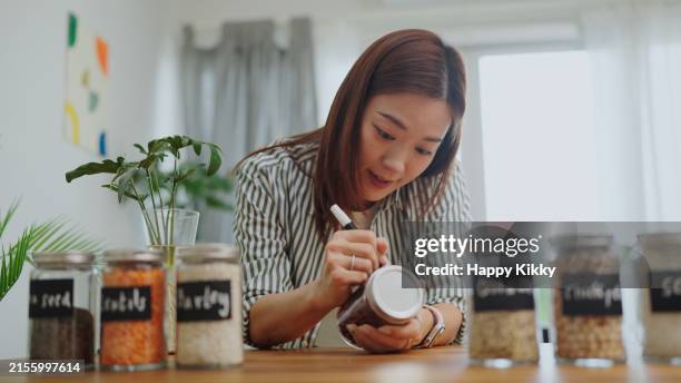asian woman hands writing 'red bean ’ with black label on a glass jar filled on a wooden counter for organized kitchen pantry storage ,zero waste lifestyle with green shopping,plastic free and sustainability at home - food in reusable containers stock pictures, royalty-free photos & images