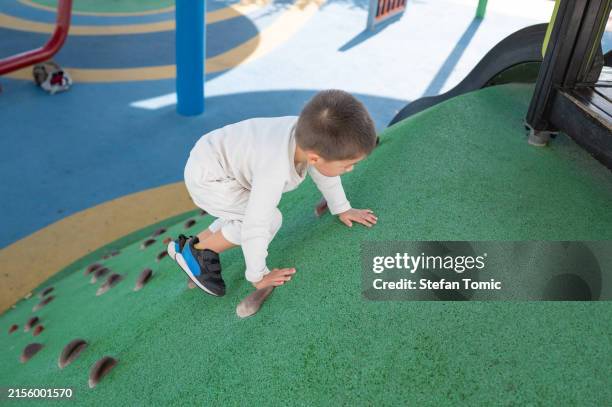young toddler climbing outdoor playground wall for fun and exercise - playground stock pictures, royalty-free photos & images