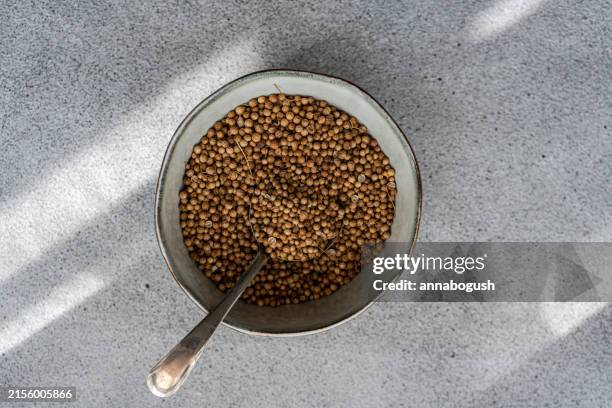 overhead view of a bowl of coriander seeds on a table - koriander stockfoto's en -beelden