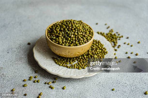 close-up of a bowl of mung beans (vigna radiata) overflowing onto a plate and table - stylisme culinaire photos et images de collection
