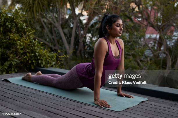 young woman practicing cobra pose yoga with eyes closed - athleisure stock-fotos und bilder