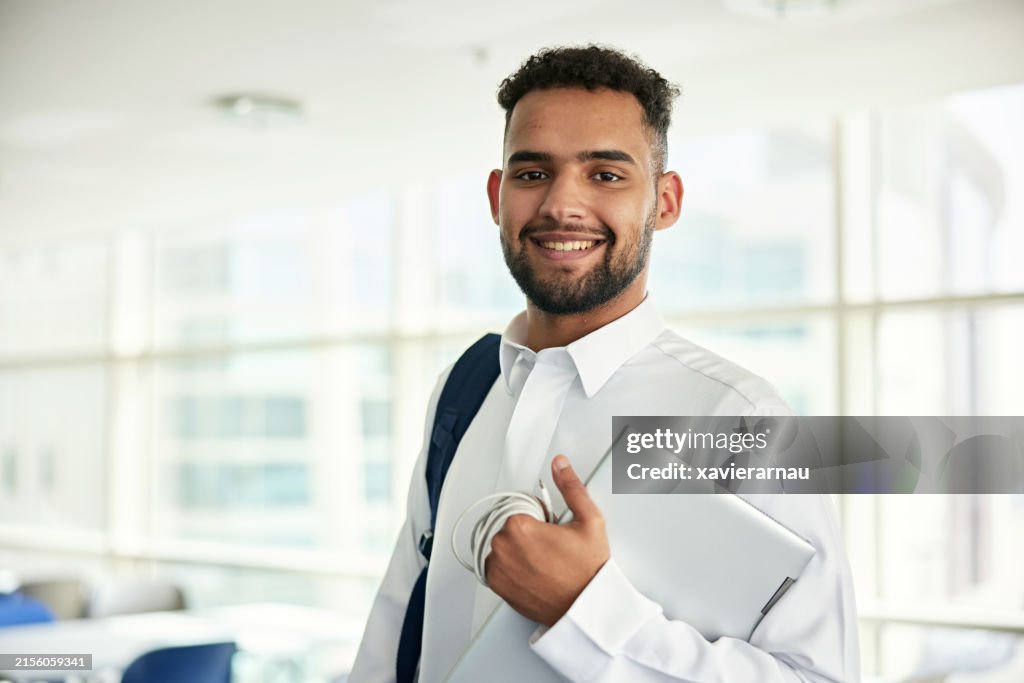 Smiling male student holding laptop
