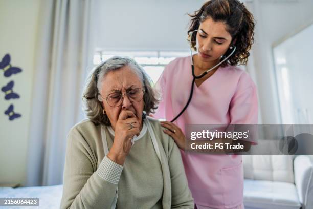 doctor examining a senior woman at nursing home - luchtweginfectie stockfoto's en -beelden