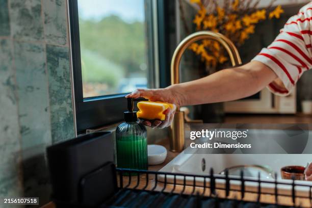 a woman's hand using a dispenser to get washing-up liquid onto a sponge - soap dispenser stock pictures, royalty-free photos & images
