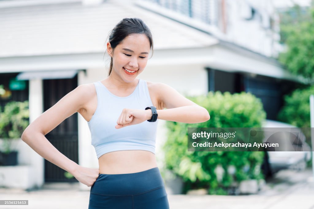 Beautiful healthy Asian woman wearing sportswear is checking her heart health. The body's calorie burning level via a smart watch after morning exercise.