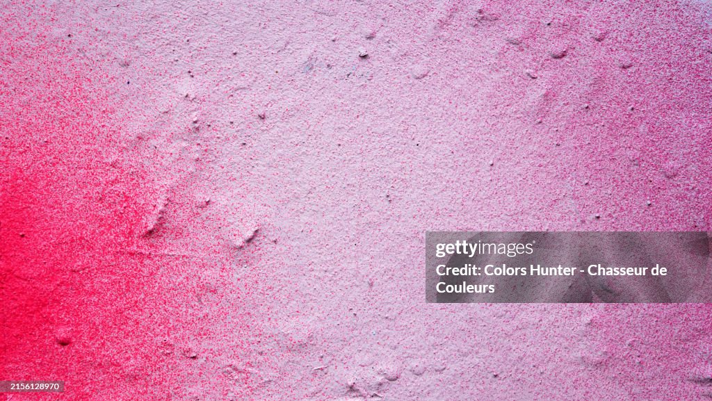 Pink spray paint on a textured white wall. Macro photograph of the facade of a house in Paris, France. Sunlight. Natural colors.