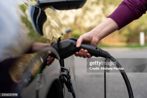 latin woman charging an electric vehicle at home - posto de carregamento de veículos elétricos imagens e fotografias de stock