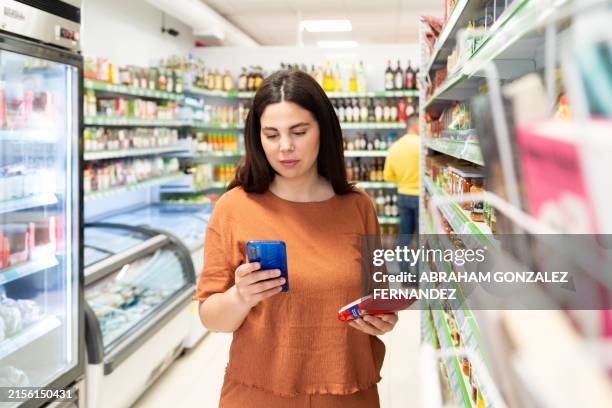 woman using phone standing in the supermarket - calcium stock pictures, royalty-free photos & images