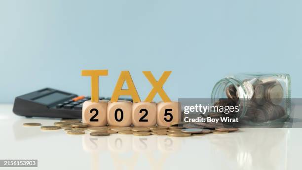 Business and tax concept. Wooden blocks spelling out TAX 2025, surrounded by coins and a calculator.  Tax deduction planning. Financial research, government taxes and calculation tax return.