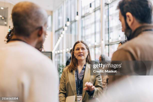 female entrepreneur explaining while standing with delegates during networking event at convention center - evento dello spettacolo foto e immagini stock