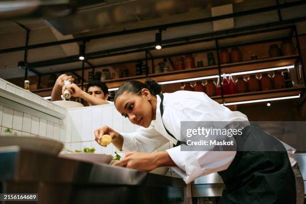 low angle view of female chef squeezing lemon on salad with male coworker seasoning at commercial kitchen - garniture photos et images de collection